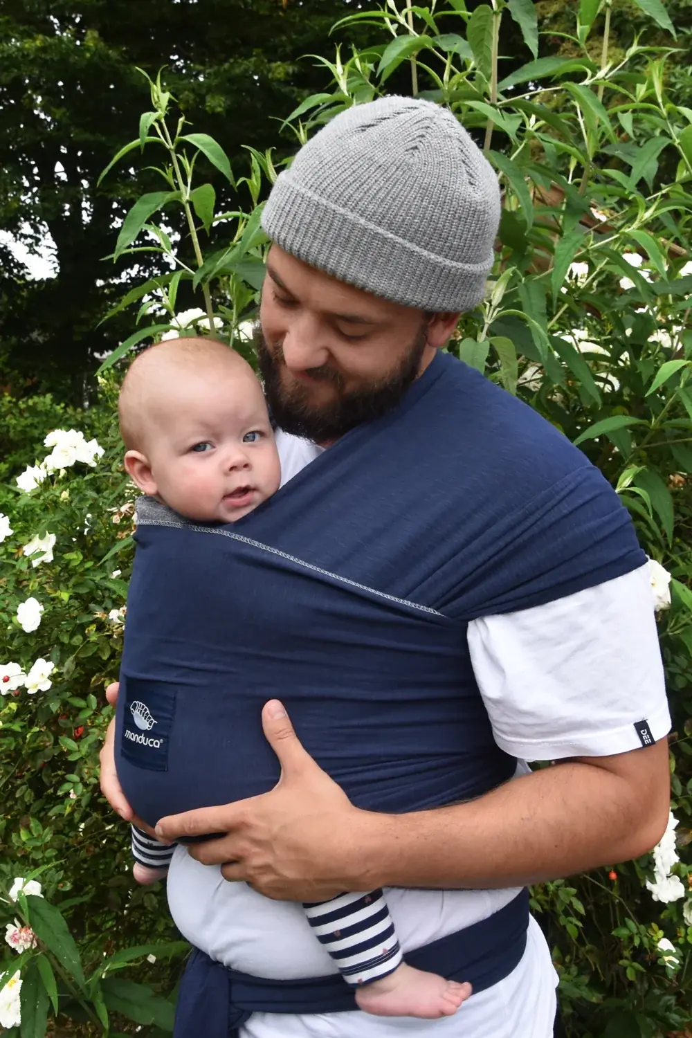 Mann trägt Baby vorne im manduca Sling Babytragetuch Navy im Garten