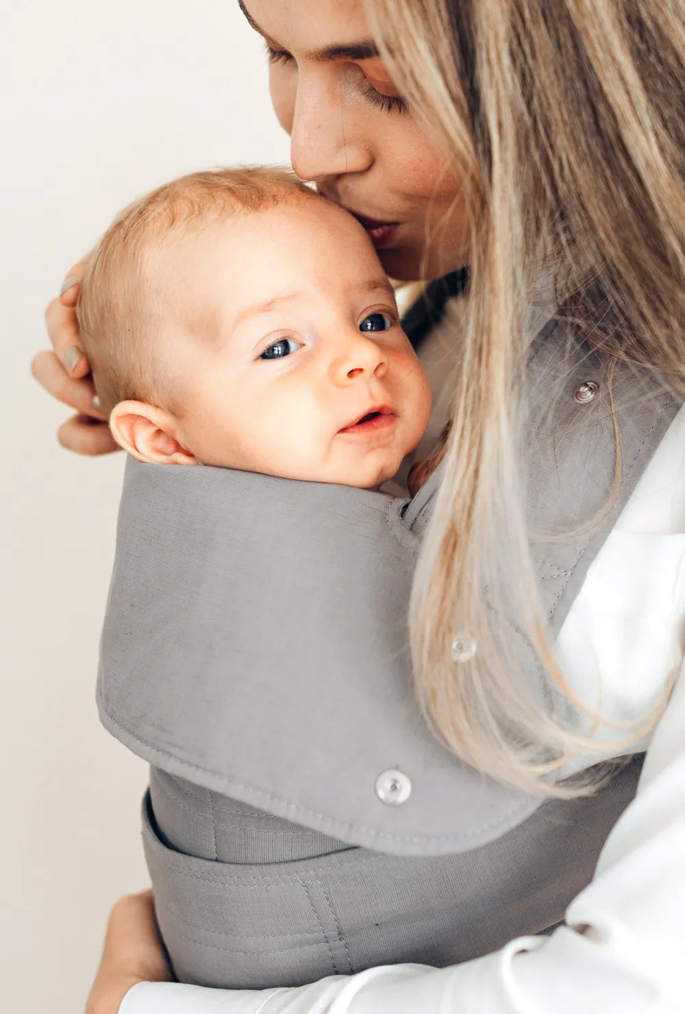 Nahaufnahme: Mutter küsst Baby in der marsupi breeze Babytrage in Hellgrau