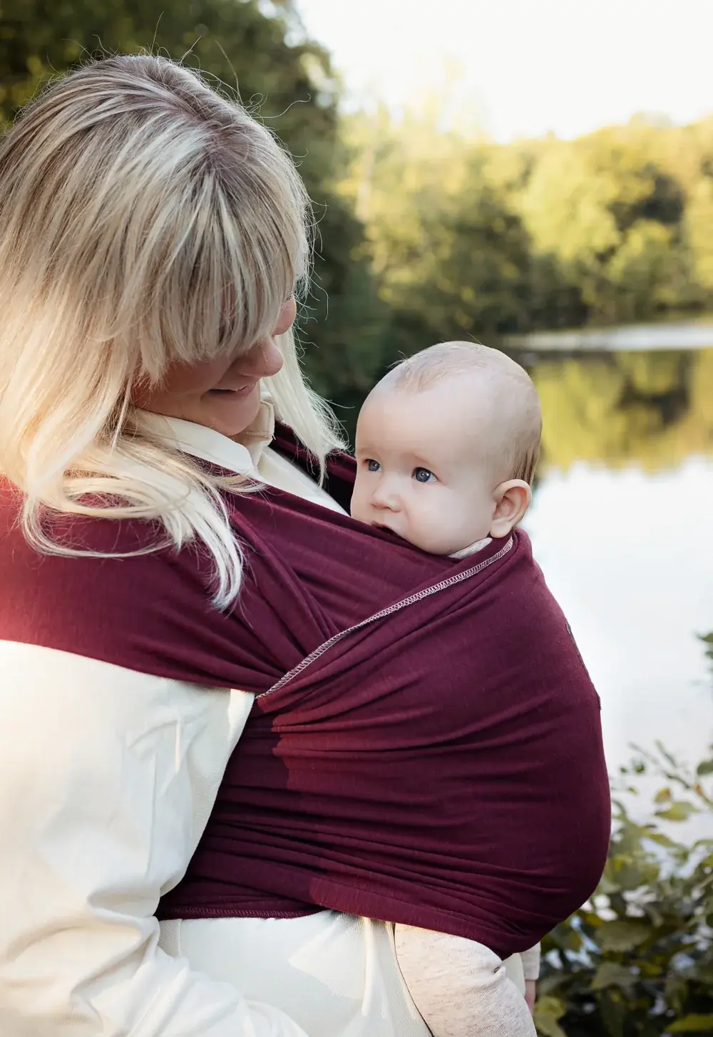 Nahaufnahme: Baby im manduca Sling Babytragetuch Berry, getragen von Frau am See