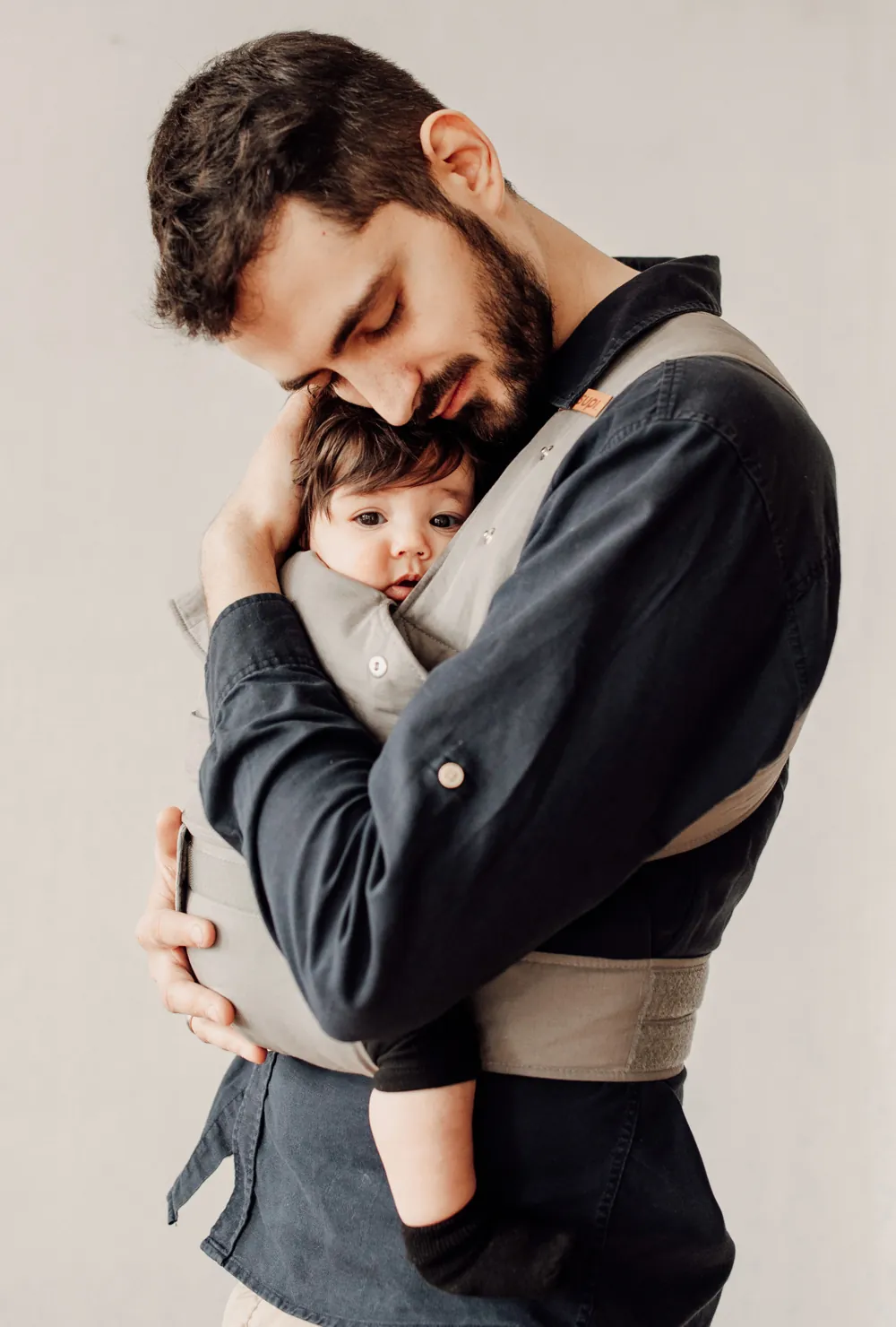 Vater hält Baby in der marsupi breeze Babytrage in Hellgrau – seitliche Aufnahme