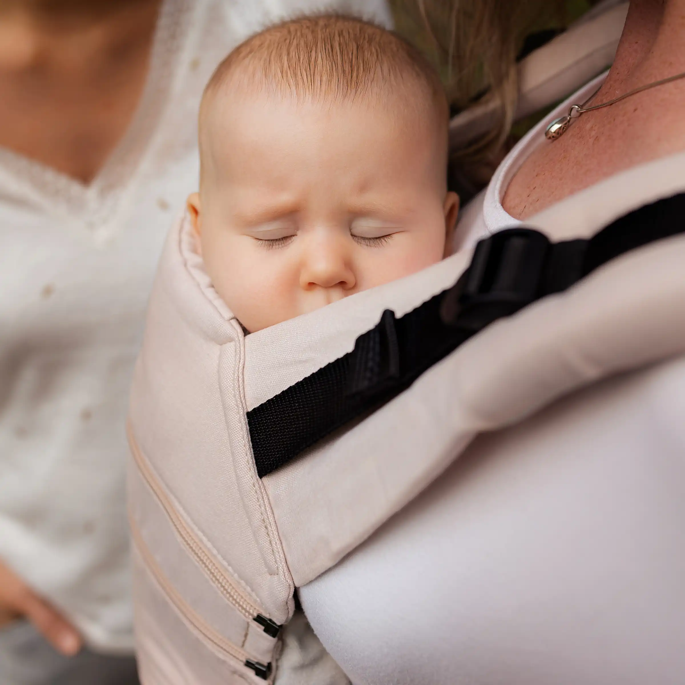 Schlafendes Baby in einer hellen Babytrage nah an einer tragenden Person.