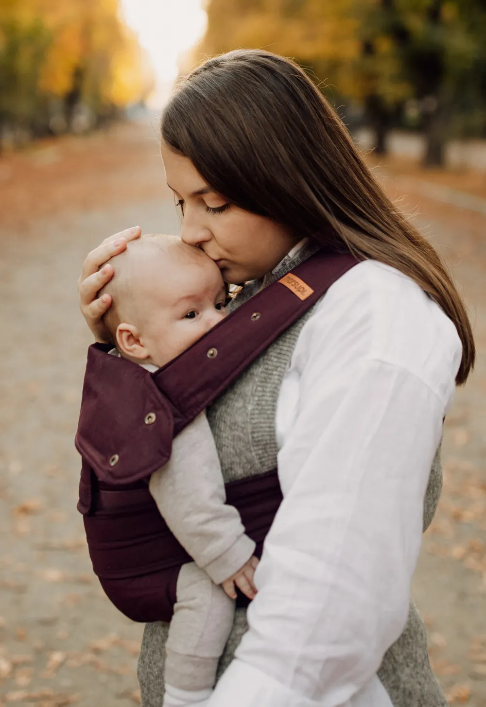 Mutter küsst Baby in der Marsupi Classic 2 Babytrage Berry – inniger Moment im Park