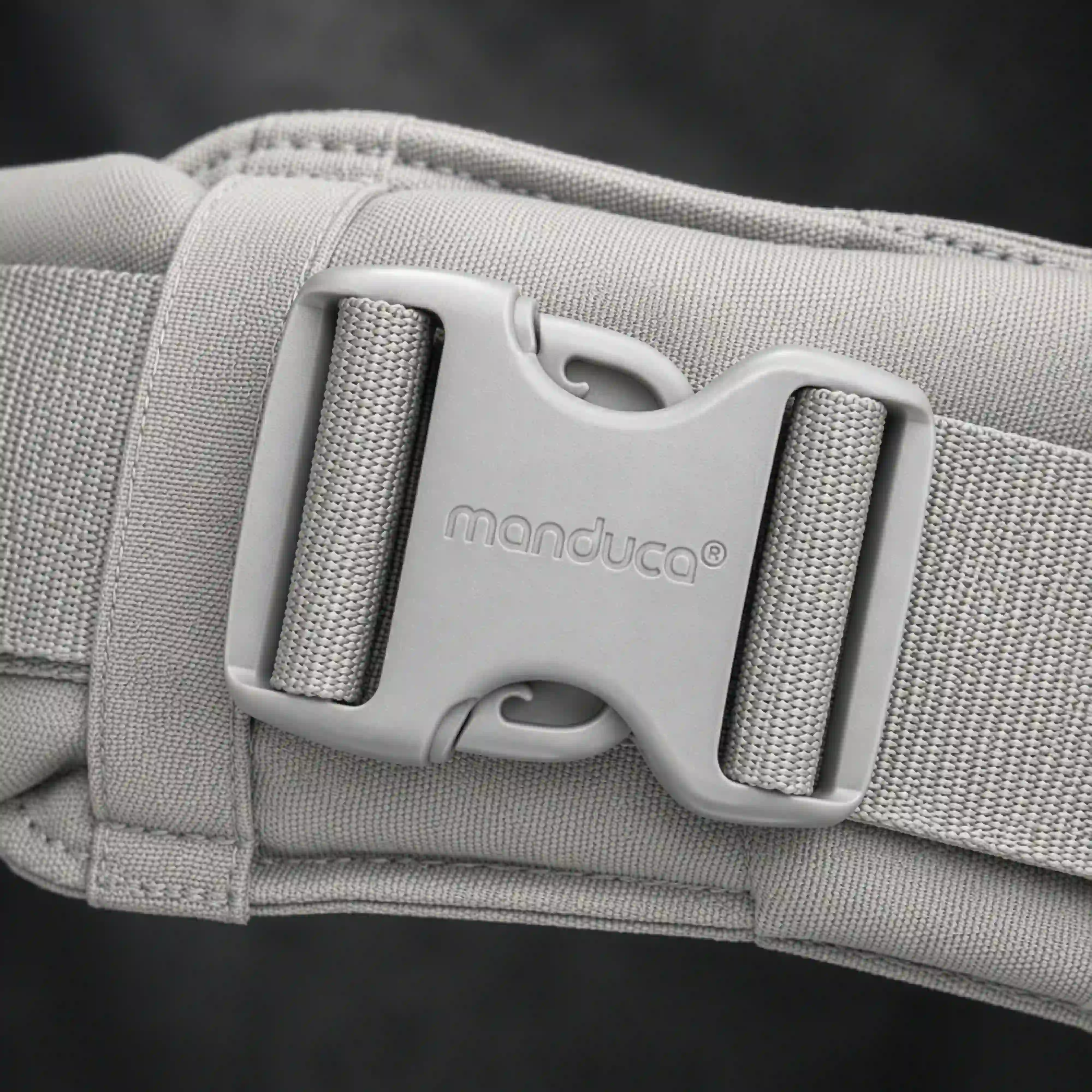 Ein Close up des Schriftzuges manduca auf einer Schnalle von der manduca XT Babytrage in monochrome Cloud