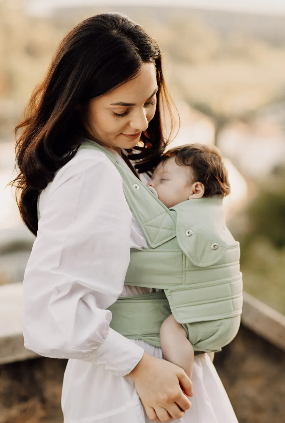 Frau trägt schlafendes Baby in der Marsupi Breeze Babytrage Pistachio – seitliche Ansicht draußen