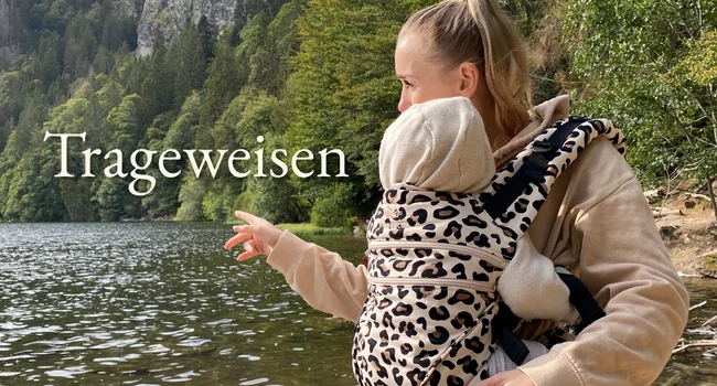 Mutter trägt baby in der manduca babytrage und zeigt auf einen Fluss