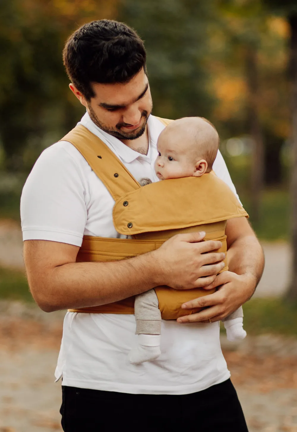 Papa trägt Baby vorne im Marsupi Classic 2 Butterscotch im Park
